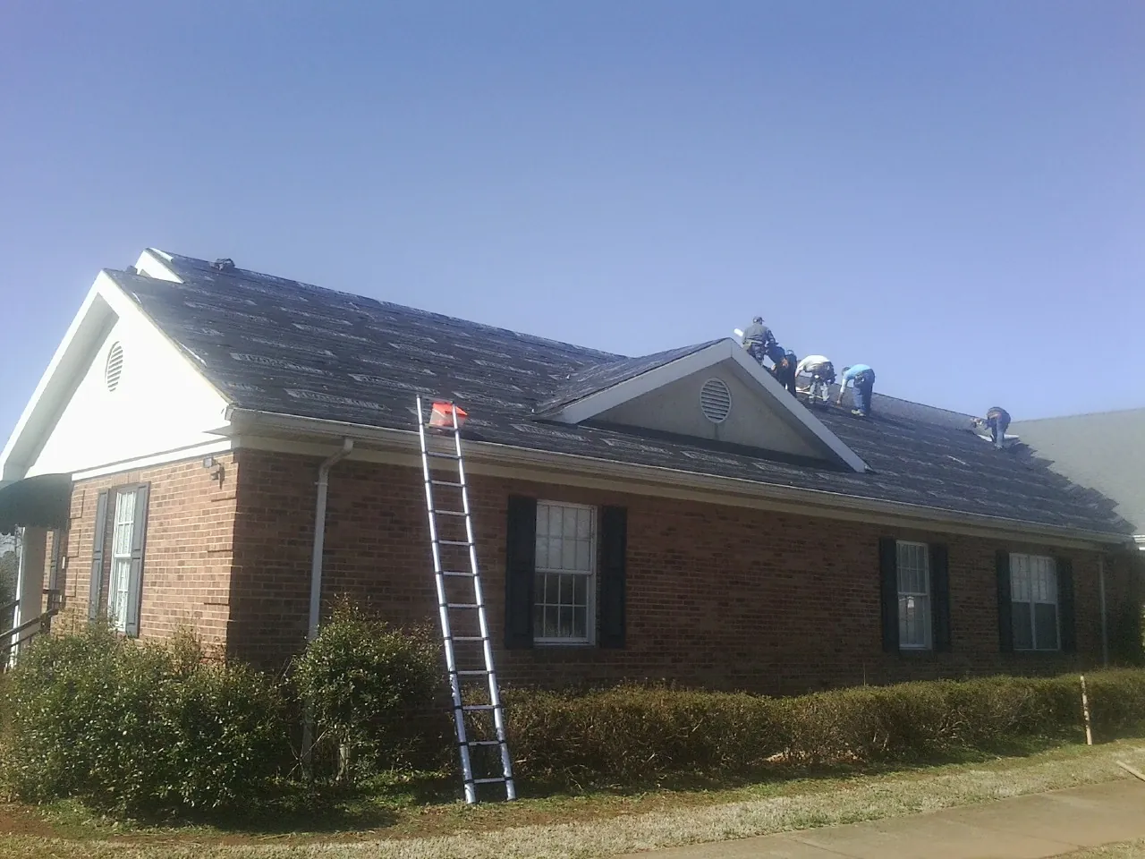 Crew tearing shingles off a brick ranch roof with a ladder set — Metal Roof Repair work by our crew in Jamestown
